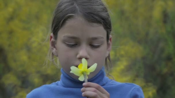 Retrato de um menino na primavera com uma flor de narciso amarelo. Rapaz abandonado a cheirar narciso de flores. O rosto do menino adolescente com uma flor na mão . — Vídeo de Stock