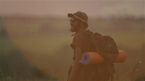 Un turista con una mochila y una cámara al atardecer en el campo. Barbudo viajero hombre hace selfie al atardecer . — Vídeos de Stock