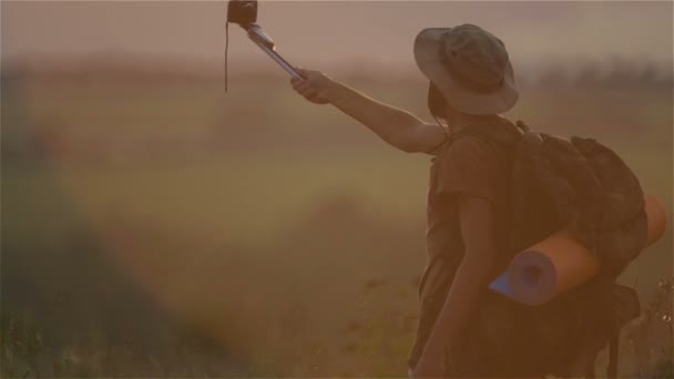 Un turista con una mochila y una cámara al atardecer en el campo. Barbudo viajero hombre hace selfie al atardecer . — Vídeo de stock