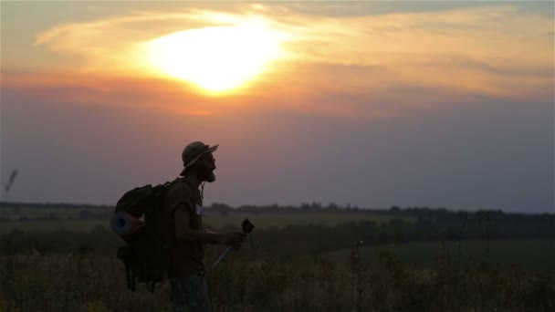 Un turista con una mochila y una cámara al atardecer en el campo. Barbudo viajero hombre hace selfie al atardecer . — Vídeos de Stock