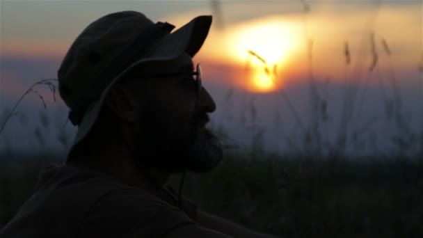 Un turista con una mochila y una cámara al atardecer en el campo. Barbudo viajero hombre hace selfie al atardecer . — Vídeos de Stock