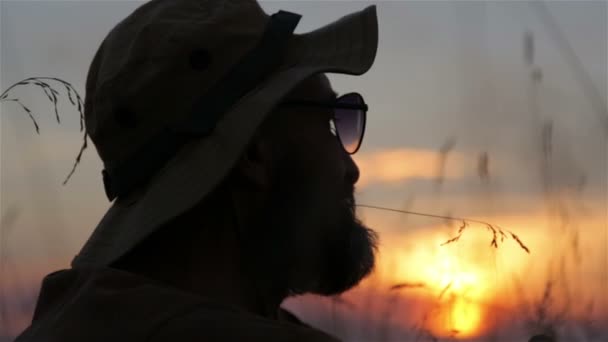 Um turista com uma mochila e uma câmera ao pôr do sol no campo. Homem barbudo viajante faz selfie ao pôr do sol . — Vídeo de Stock