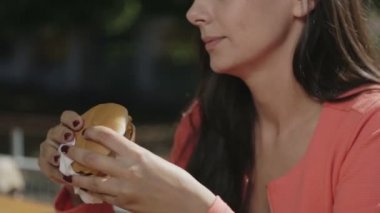 Elinde bir hamburger ile kız yakın çekim portresi. Güzel bir genç kadın bir kafede hamburger yemek.