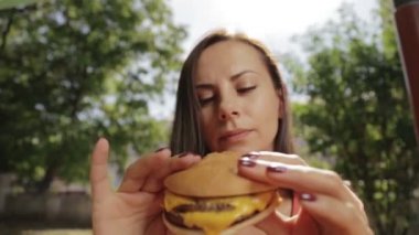 Elinde bir hamburger ile kız yakın çekim portresi. Güzel bir genç kadın bir kafede hamburger yemek.