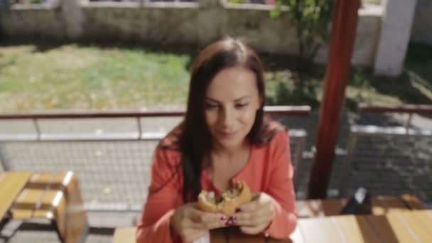 Retrato de uma menina close-up com um hambúrguer na mão. Uma jovem mulher bonita a comer um hambúrguer num café. Comida, Fast Food, Nutrição . — Vídeo de Stock