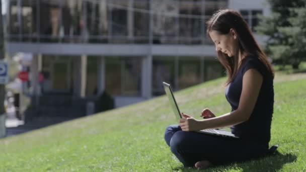 Young beautiful woman in the park with a laptop. Beautiful brunette typing on a laptop sitting on the lawn. People, Nature, Technology. — Stock Video