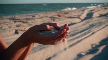 Female hand with sea sand on the beach. The sand is slowly pouring out of the girl's hand.