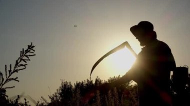 Bir adam bir el tırpanı ile çimleri biçer, siluet. 