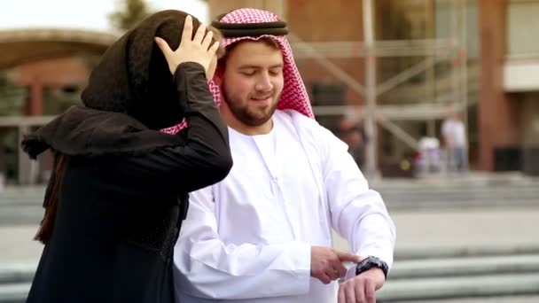 Pareja joven en ropa árabe en el fondo de la ciudad. Retrato de una hermosa pareja joven en el vestido nacional árabe. Hombre árabe mirando su reloj . — Vídeos de Stock