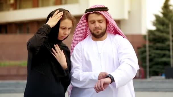 Junges Paar in arabischer Kleidung vor dem Hintergrund der Stadt. Porträt eines schönen jungen Paares im arabischen Nationalkleid. Araber schaut auf seine Uhr. — Stockvideo
