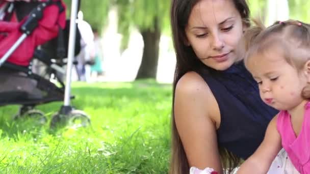 Madre joven con el bebé en un parque de la ciudad.Madre jugando con el bebé en el parque en la pradera. Familia en el parque de vacaciones. Mamá con una niña en la naturaleza . — Vídeos de Stock