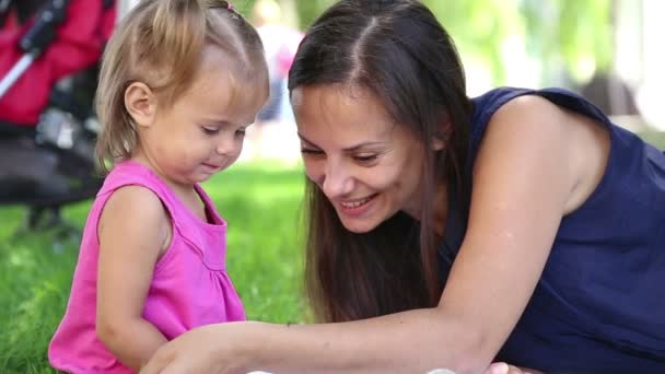 Mãe nova com bebê em um parque da cidade.Mãe brincando com bebê no parque na grama.Família no parque de férias. Mãe com uma menina na natureza . — Vídeo de Stock