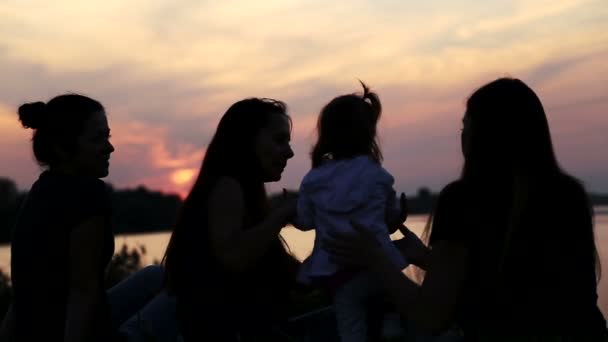 Petite amie avec bébé au coucher du soleil.Silhouette de trois filles avec un enfant.Trois mères avec bébé sur nature.Jeune mère avec bébé au lac au coucher du soleil . — Video