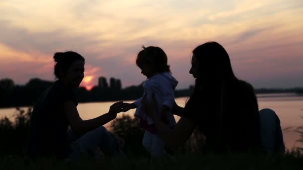 Vriendin met baby op sunset.silhouette van drie meisjes met een child.three moeders met baby op nature.young moeder met baby aan het meer bij zonsondergang. — Stockvideo