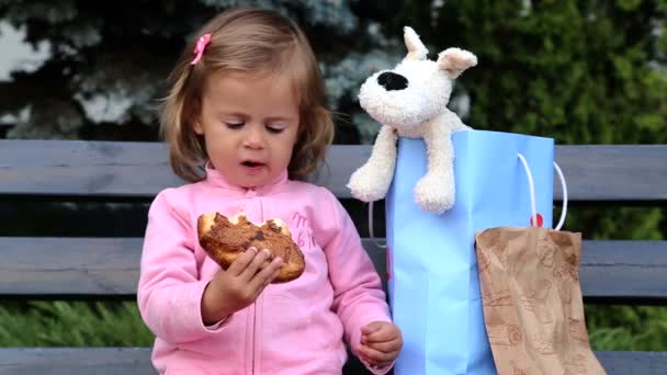 Niña comiendo un bollo.Niño comiendo pasteles en la tienda.Niño pequeño lo come con sabor.Retrato de una niña que come un panecillo . — Vídeo de stock