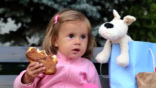 Kleines Mädchen isst ein Häschen.Kind isst Gebäck im Laden.kleines Kind isst es genüsslich.Porträt eines kleinen Mädchens, das einen Muffin isst. — Stockvideo