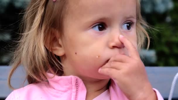 Niña comiendo un bollo.Niño comiendo pasteles en la tienda.Niño pequeño lo come con sabor.Retrato de una niña que come un panecillo . — Vídeo de stock