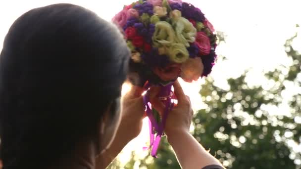 Brautstrauß in der Sonne. Brautstrauß in den Händen der Braut bei Sonnenuntergang. Mädchen mit Blumenstrauß im Sonnenlicht. — Stockvideo