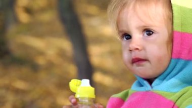 Çocuk maden suyu içiyor. İçme suyu doğada küçük bir kızdır. Küçük parlak giysiler içinde içme suyu bir şişe sonbahar parkta kızdır. Duyguları çocuk portre.