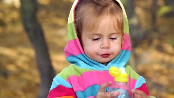 아이 미네랄 워터를 마시고 있다. 어린 소녀는 자연에서 식 수입니다. 밝은 옷에 어린 소녀가을 공원에 한 병에서 식 수입니다. 감정 자식 근접 촬영. — 비디오