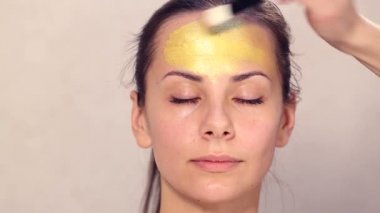 Güzel kızın yüzüne kozmetik maske uygulanıyor. Yüz maskeleri kozmetik kullanımı. Kozmetik altın maske yüzünde uygulanıyor. Dekoratif kozmetik. Kız portresi yakın çekim bir Güzellik Salonu.