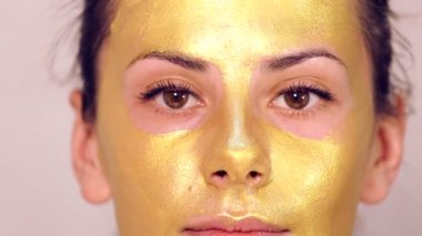 Güzel kızın yüzüne kozmetik maske uygulanıyor. Yüz maskeleri kozmetik kullanımı. Kozmetik altın maske yüzünde uygulanıyor. Dekoratif kozmetik. Kız portresi yakın çekim bir Güzellik Salonu.