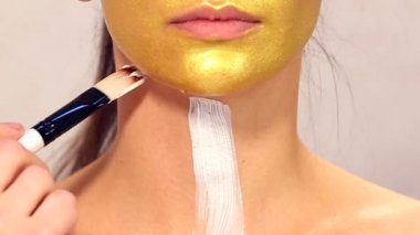 Güzel kızın yüzüne kozmetik maske uygulanıyor. Yüz maskeleri kozmetik kullanımı. Kozmetik altın maske yüzünde uygulanıyor. Dekoratif kozmetik. Kız portresi yakın çekim bir Güzellik Salonu.