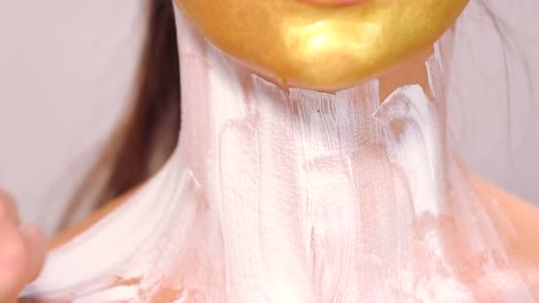 Εφαρμογή καλλυντικά μάσκα στο πρόσωπό της όμορφο κορίτσι. Χρήση του προσώπου μάσκες στην κοσμητολογία. Εφαρμογή καλλυντικά χρυσή μάσκα στο πρόσωπο. Διακοσμητικά Καλλυντικά. Προσωπογραφία του κοριτσιού από κοντά στο σαλόνι ομορφιάς. — Αρχείο Βίντεο