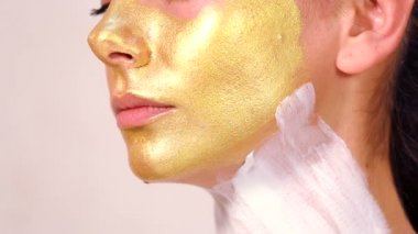 Güzel kızın yüzüne kozmetik maske uygulanıyor. Yüz maskeleri kozmetik kullanımı. Kozmetik altın maske yüzünde uygulanıyor. Dekoratif kozmetik. Kız portresi yakın çekim bir Güzellik Salonu.