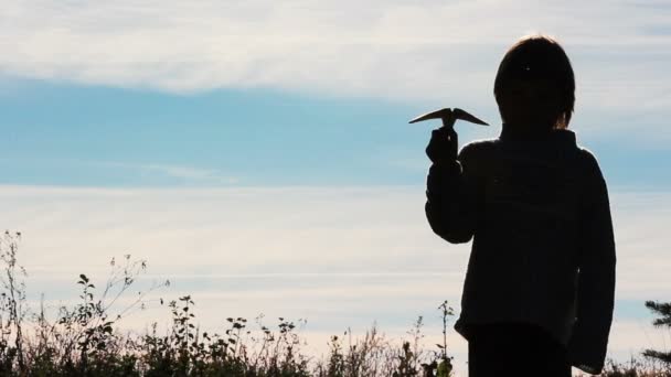 Silhouette di un ragazzo che gioca con un aereo di carta.Ragazzo solitario che gioca all'aperto.Il bambino inizia aereo su sfondo cielo . — Video Stock