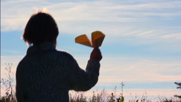 Silhouette di un ragazzo che gioca con un aereo di carta.Ragazzo solitario che gioca all'aperto.Il bambino inizia aereo su sfondo cielo . — Video Stock