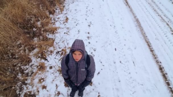 Niño adolescente caucásico que viaja en invierno (vista superior). El niño va en una carretera de invierno a través de los campos (vista superior). Propósito adolescente supera la manera difícil . — Vídeos de Stock