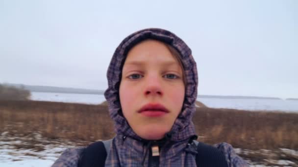 Chłopiec kaukaski patrząc na kamery, przędzenia. Dziecko, trzymając aparat i strzela sobie w polu zima. Close-up portret. Ruch w okręgu. — Wideo stockowe