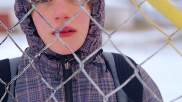 Caucasian boy at an abandoned farm in the winter. The child is a teenager walking on the old farm. Portrait of a boy, close-up through the bars of the fence. — Stock Video