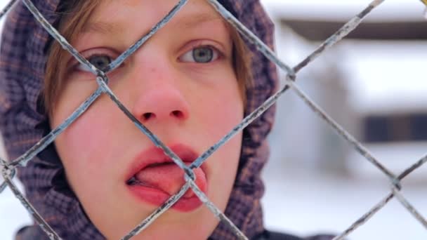 Caucasian boy at an abandoned farm in the winter. The child is a teenager walking on the old farm. Portrait of a boy, close-up through the bars of the fence. — Stock Video