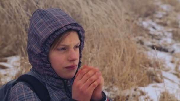 Kaukasiska pojke tonåring värma frusna händer. Barnet frös promenader i naturen på vintern. Porträtt av tonårspojke närbild, värma händerna. — Stockvideo