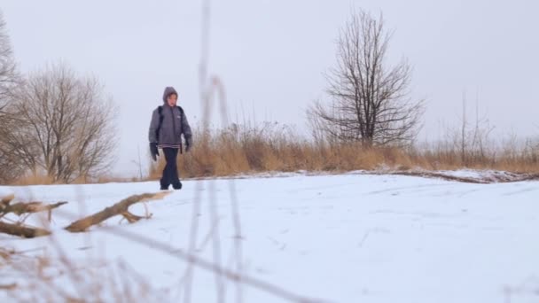 Chłopiec kaukaski nastolatek podróży w zimie. Dziecko idzie na zimą droga przez pola. Celowe nastolatek pokonuje skórze. — Wideo stockowe