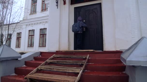 Niño caucásico cerca del edificio de la escuela del pueblo. Un niño camina y sube cerca de la vieja casa. País chico adolescente . — Vídeos de Stock