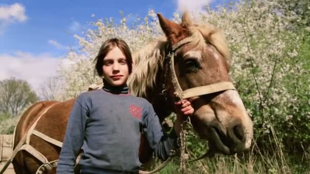 Kaukasiska pojke tonåring med en häst på naturen. Landsbygdens barn med en sällskapsdjur favorithäst. Pojken hand tar om sina husdjur, en favorit häst. Människor, natur, djur. — Stockvideo