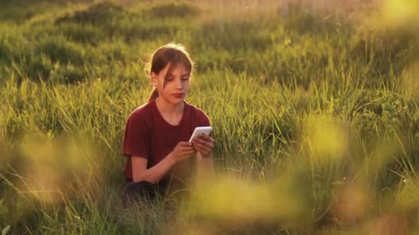 Niño caucásico con el teléfono en la naturaleza.Niño adolescente con un teléfono inteligente al atardecer. Naturaleza, personas y tecnología . — Vídeos de Stock