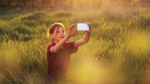 Kaukasiska pojke med telefonen på naturen. Pojke tonåring med en smartphone i solnedgången. Pojke med telefonen fotograferar solnedgången. Natur, människor och teknik. — Stockvideo