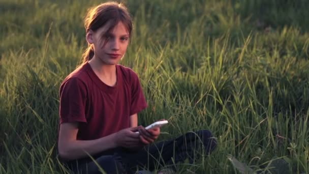 Niño caucásico con el teléfono en la naturaleza.Niño adolescente con un teléfono inteligente al atardecer. Naturaleza, personas y tecnología . — Vídeo de stock