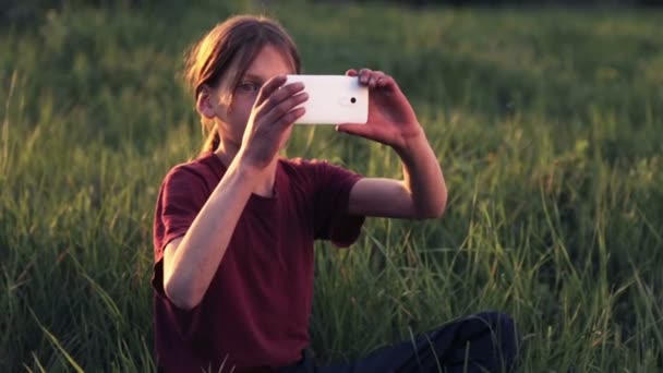 性質の携帯電話で白人少年。夕暮れ時のスマート フォンで少年 10 代。携帯電話写真夕日と少年。自然、人、および技術. — ストック動画