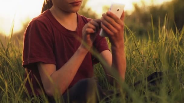 Niño caucásico con el teléfono en la naturaleza.Niño adolescente con un teléfono inteligente al atardecer. Naturaleza, personas y tecnología . — Vídeo de stock