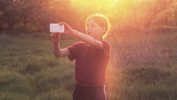 Niño caucásico con el teléfono en la naturaleza.Niño adolescente con un teléfono inteligente al atardecer. Naturaleza, personas y tecnología . — Vídeos de Stock