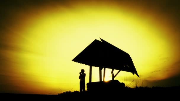 Silhouet van een jongen op zonsondergang op de oude waterput. Silhouet van een kind in een veld bij zonsondergang. Tiener jongen met het gereedschap op de natuur. Natuur, kind, silhouet, zonsondergang. — Stockvideo