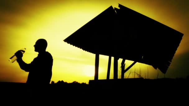 Silhouette eines Mannes mit einer Flasche Wasser bei Sonnenuntergang. Mann trinkt Wasser bei Sonnenuntergang. — Stockvideo