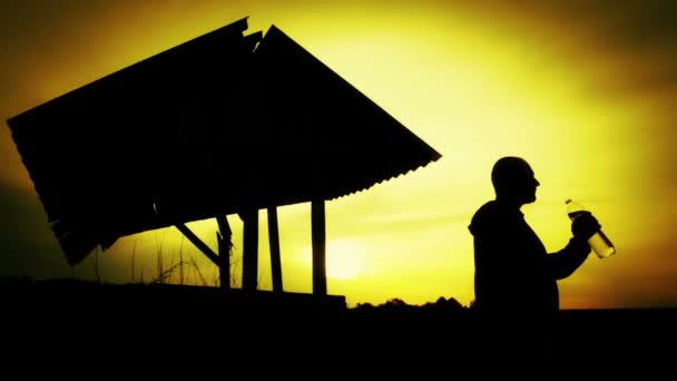 Silueta de un hombre con una botella de agua al atardecer. El hombre bebe agua al atardecer . — Vídeos de Stock