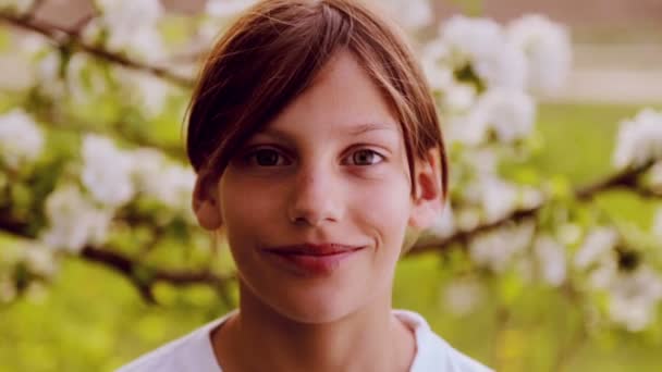 Retrato close-up, menino de pele branca no jardim da primavera. Garoto caucasiano em um jardim exuberante na primavera. O rosto da criança nas flores da primavera . — Vídeo de Stock