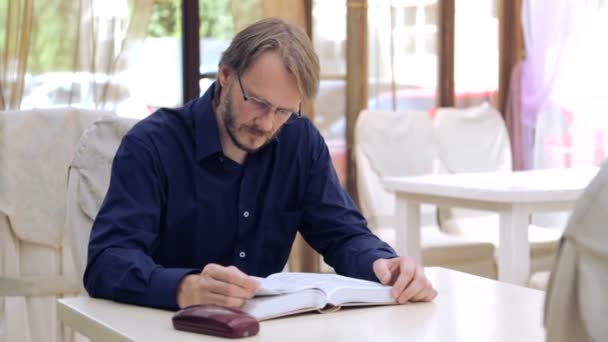 Un uomo caucasico che legge un libro al bar. Ritratto di un giovane con un libro al ristorante. Un giovanotto elegante. Istruzione, stile di vita . — Video Stock